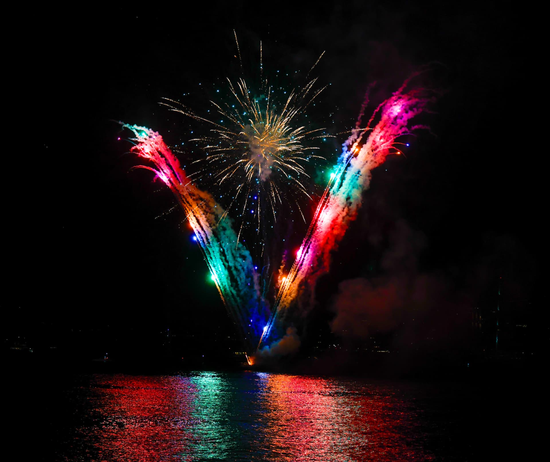 Feu d'artifice coloré tiré depuis l'eau la nuit, reflets sur la mer