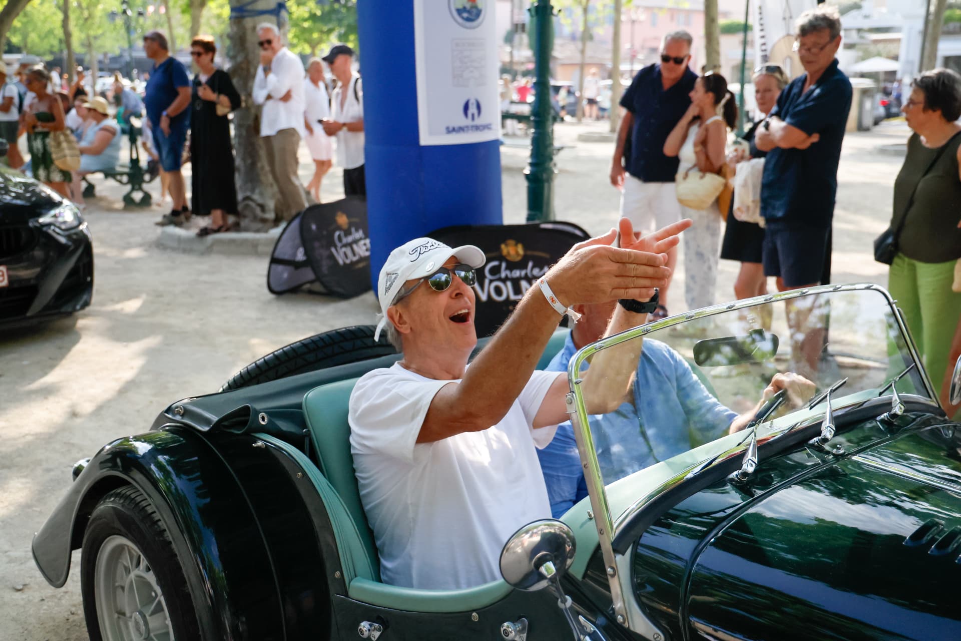 Homme saluant depuis une voiture ancienne lors d'un rassemblement en ville